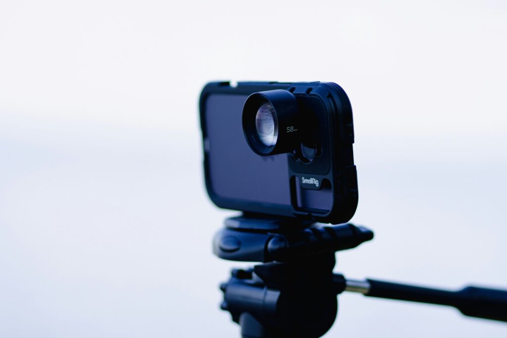 A black smartphone set up on a tripod against a white background.